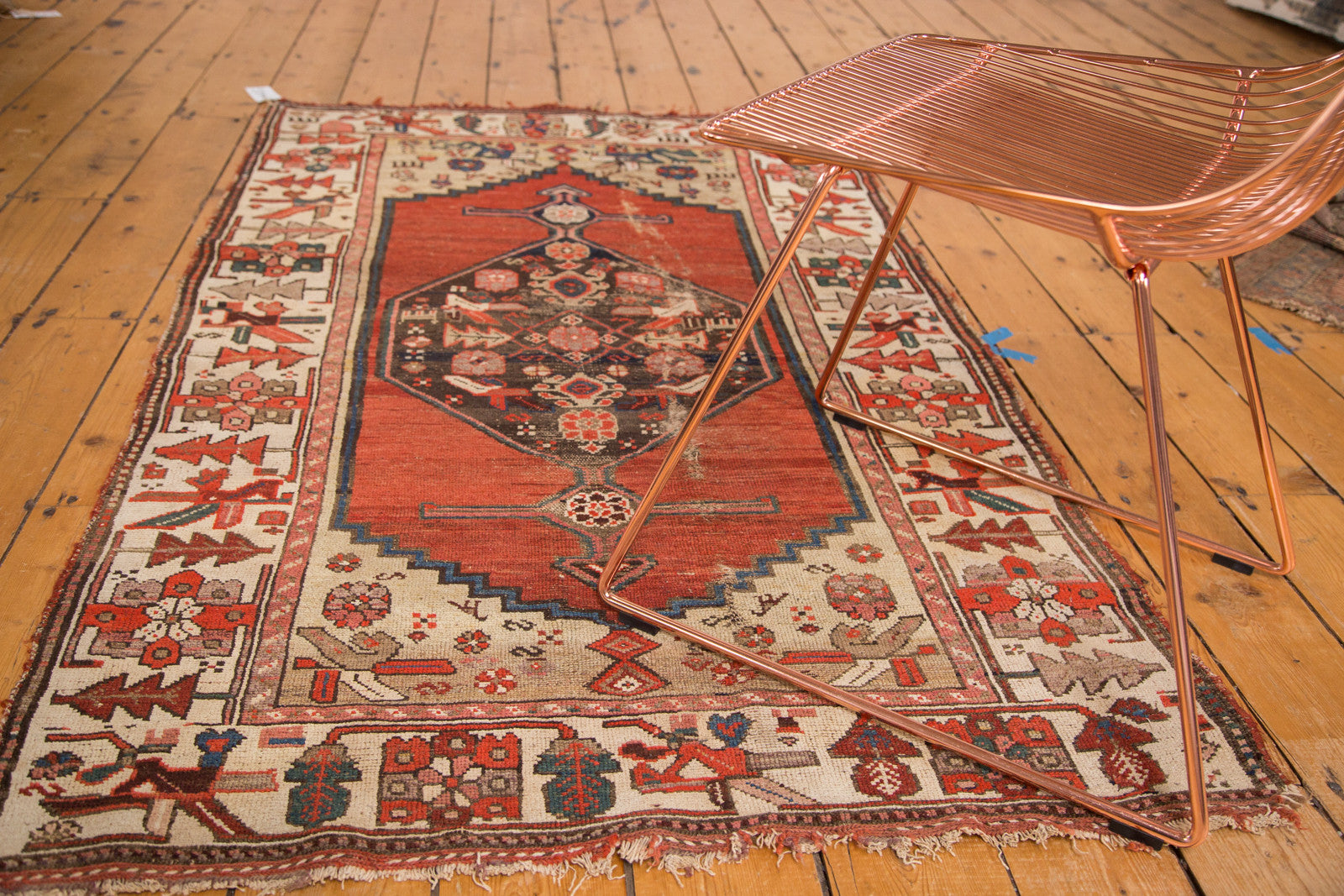 Lower corner of a distressed vintage Kurdish Hamadan rug, showing geometric birds on ivory border.